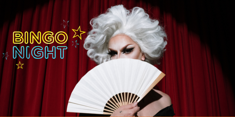 Drag queen holding a white fan in front of her face while standing on stage in front of red curtain with Bingo Night in neon overlayed