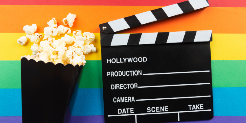 Movie clapboard and black popcorn bag on a rainbow background with LGBTQ+ flag colors