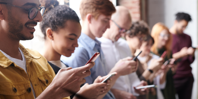 Diverse group of people standing indoors looking at their mobile phones