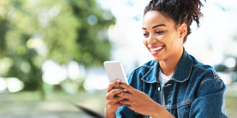 Happy African American young woman typing on her mobile phone in a park