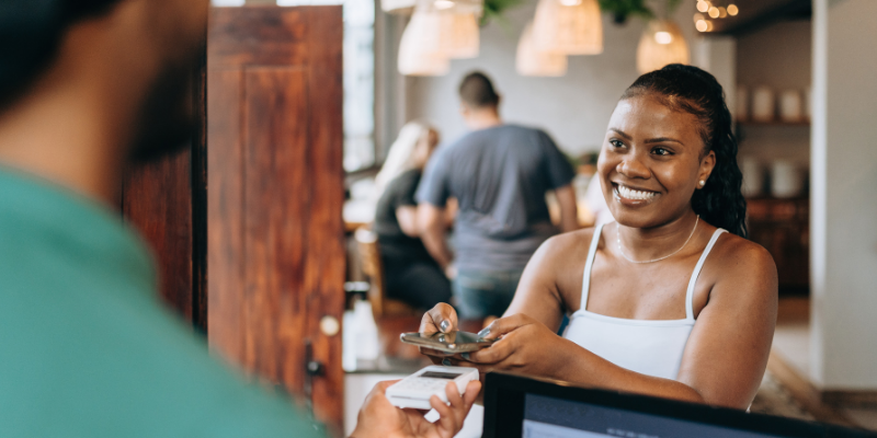 Smiling African American woman using tap-to-pay at a restaurant