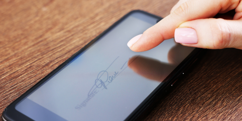 Close-up of a phone screen with an e-signature page and a womans hand signing electronically