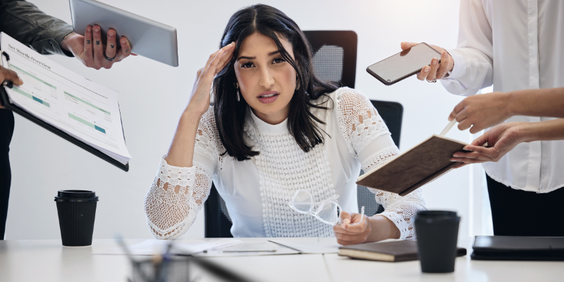 The Firefighter_ overwhelmed woman sitting at a desk while colleagues bring over reports and devices