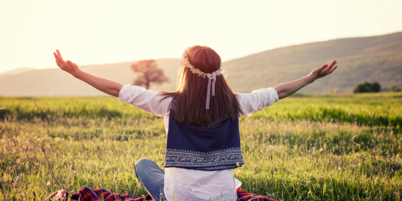 The Go-with-the-Flower_ Carefree woman sitting on a blanket with arms outstretched outdoors