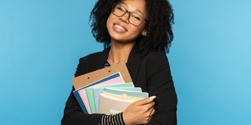 The Notebook Nostalgist_ happy student holding a stack of notebooks against a blue background