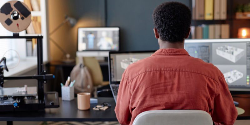 The Tech Whisperer_ person working in a design studio with multiple screens and a 3-d printer