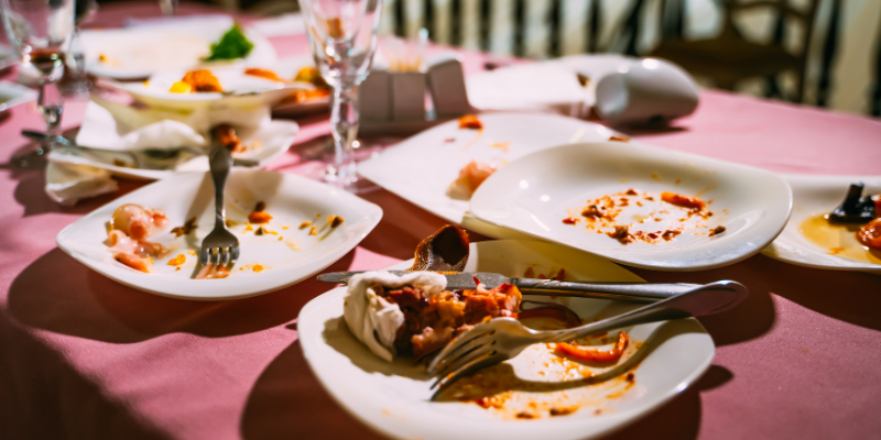 Messy table after a party with food bits left on plates and cutlery