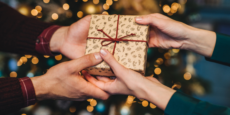 Close-up shot of two friends handing over a small gift box tied with a thin red string