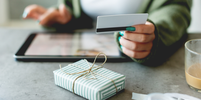 Close-up of woman hands tapping on a tablet to purchase gifts with a gift card, wrapped gift in the foreground