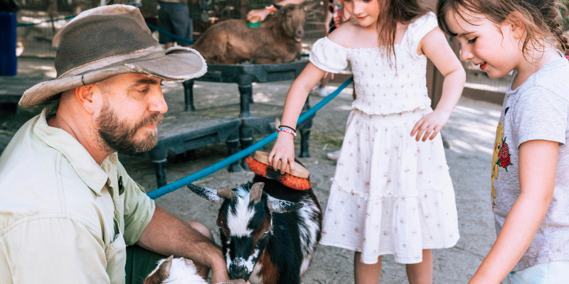 Children petting goats supervised by a park ranger at a petting zoo