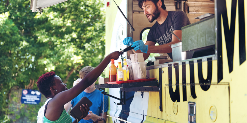 Food truck owner and chef accepting mobile payment from a woman outdoors