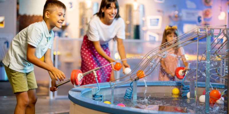 Mom with two kids at a science center playing a learning activity with water and balls