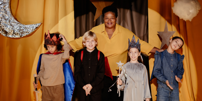 Teacher standing on stage with diverse group of children in homemade costumes for a performance