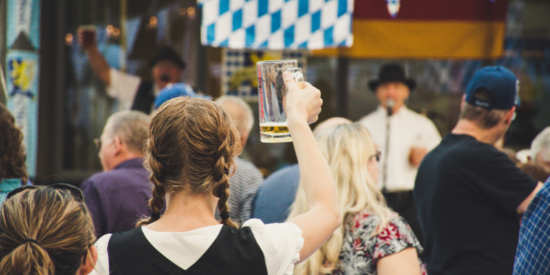 A young woman holding up almost empty stein glass to cheers at an outdoor Oktoberfest event
