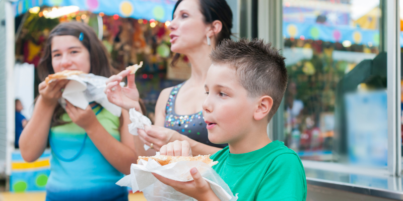 Woman and two children eating funnel cakes at a fair