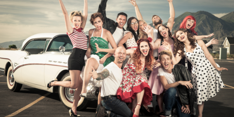 Group of friends in retro attire standing in front of a vintage car outdoors