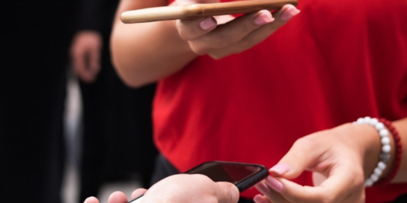 Closeup image of a woman in red shirt using her mobile phone to scan a ticket on a guests mobile phone