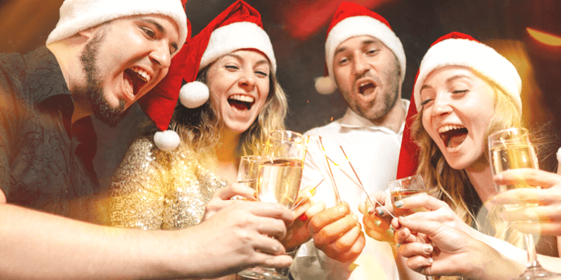 Four people wearing santa hats and cheersing champagne flutes.