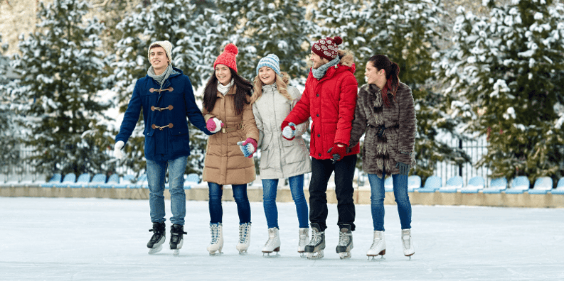 Group of five people ice skating together outdoors dressed in heavy winter clothing.