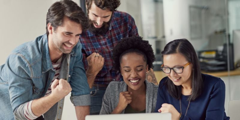 group of coworkers excitedly looking at a computer screen and smiling