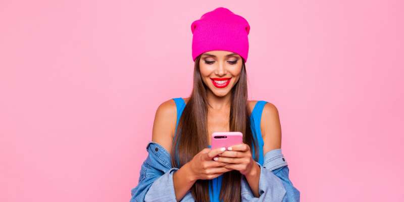 woman with bright pink hat checking phone on a light pink background