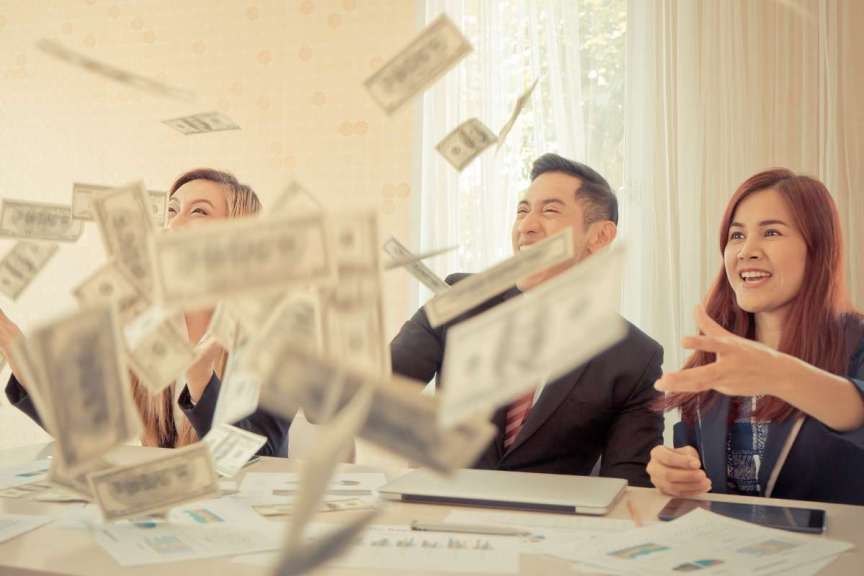 team sitting around conference table throwing money in the air