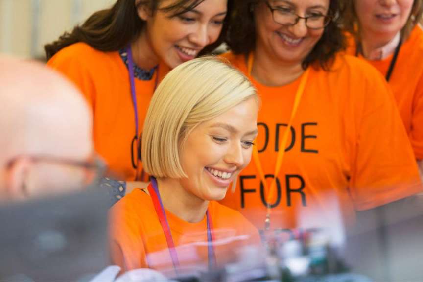 nonprofit volunteers looking over shoulder of blonde woman with short hair smiling looking at computer