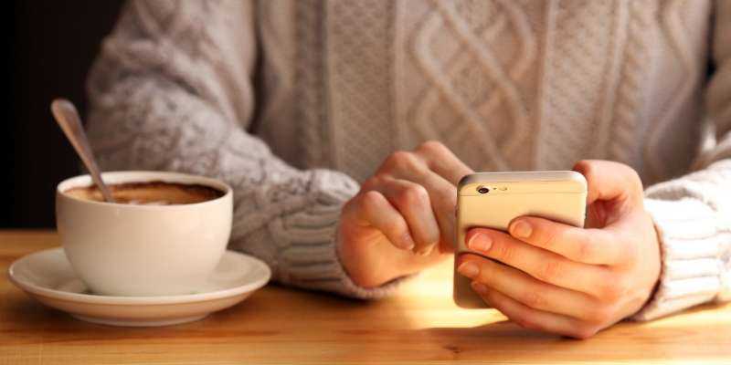 person in a sweater using their phone with a cup of coffee next to them