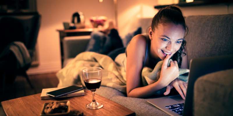 woman watching virtual event on couch with a glass of wine