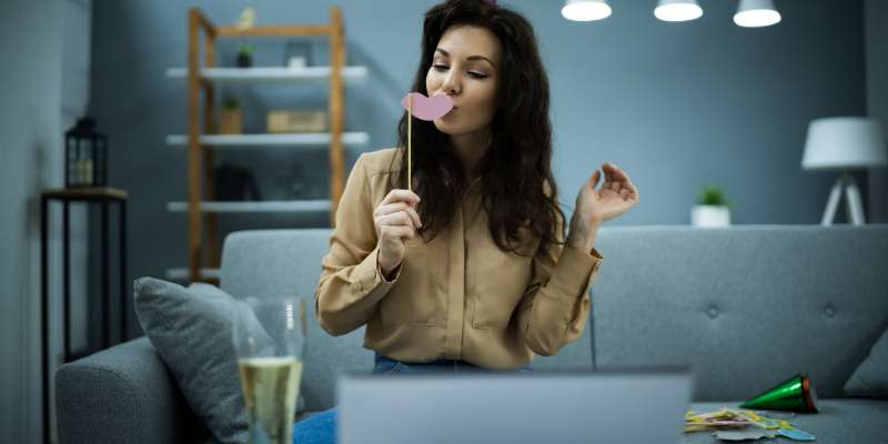 woman holding paper lips on a stick in front of mouth while on a video call