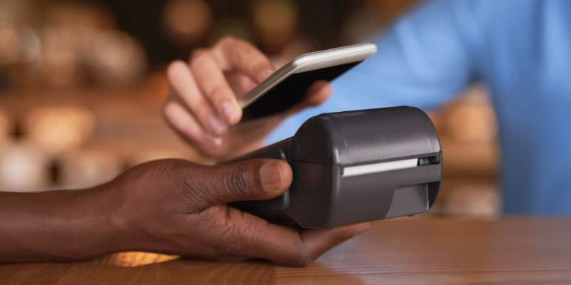hand of a person using their phone to complete a tap-to-pay transaction while another hand holds the card terminal