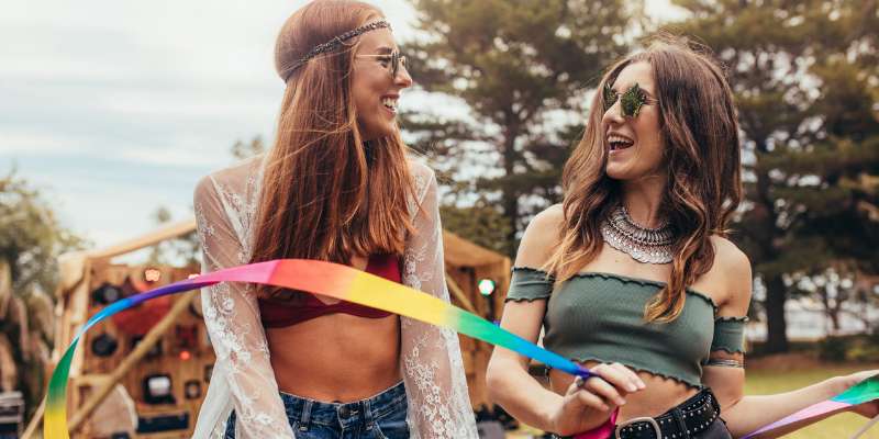 two female friends playing with rainbow ribbon at festival