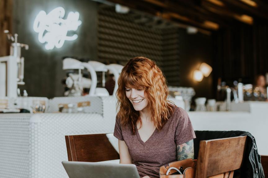 happy woman with red hair working on laptop in coffee shop
