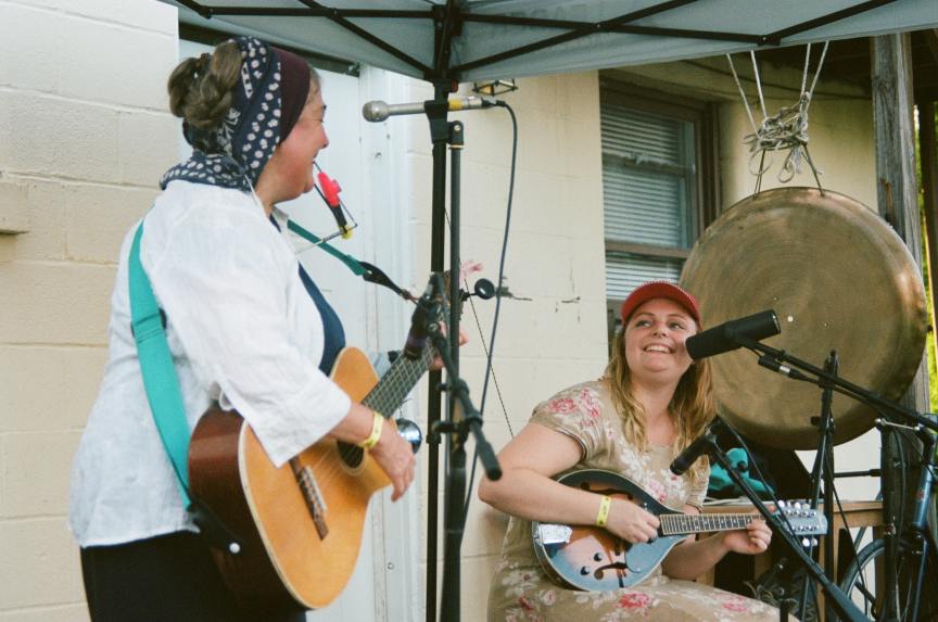 two women playing guitar outdoors and singing into microphones