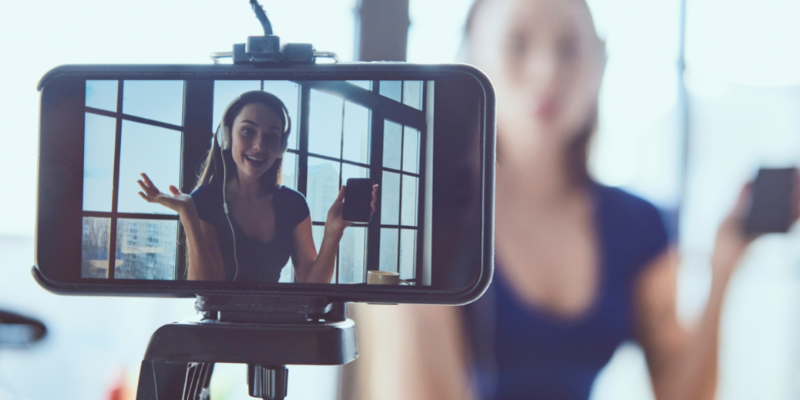 Woman talking to a phone with headphones on while it video records her.