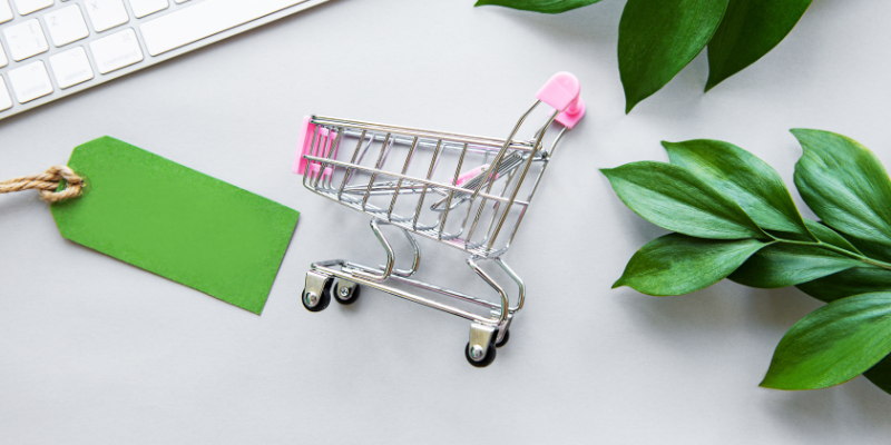 Miniature shopping cart with a small green shopping tag to the left of it.