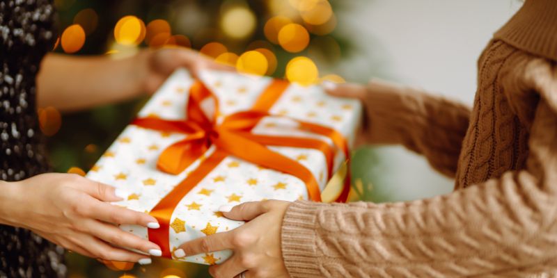 the hands of two women exchanging a gift with star wrapping paper and an orange bow