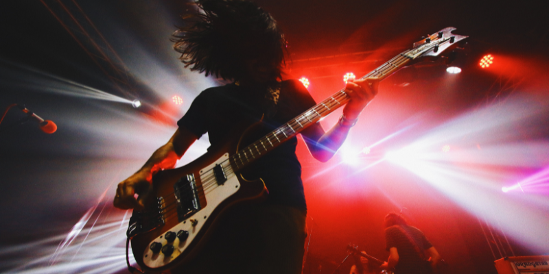 Man holding a guitar on stage at a rock concert while lights flash behind him.