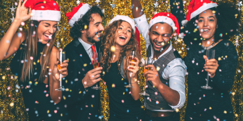 Five people wearing Santa hats and cheersing drinks.