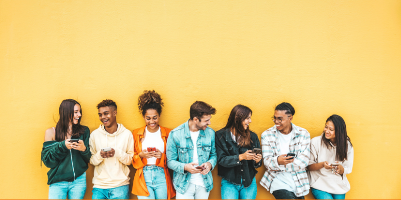 Diverse group of young people using mobile phones against a yellow background