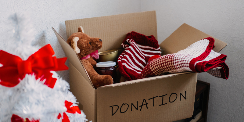 Various things in a box for holiday charity drive, including a teddy bear, warm socks and tea towel