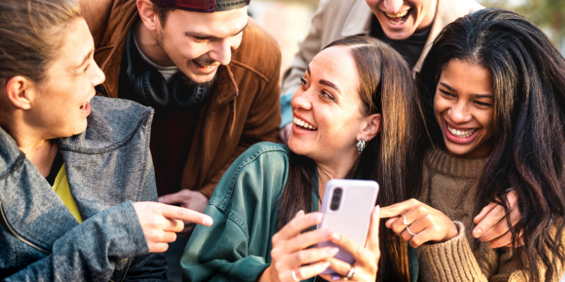 Happy group of multicultural young people looking at friend's mobile phone outdoors