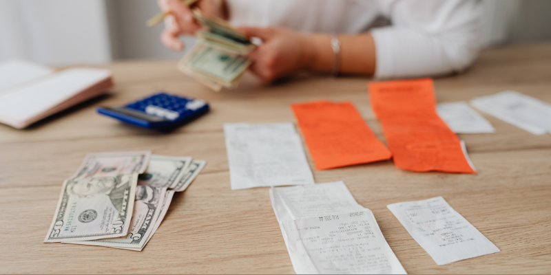 Person paying bills counting cash with a calculator and receipts on the table