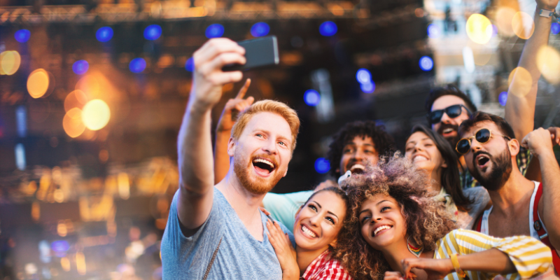 Group of friends taking a selfie in front of a stage at a music festival