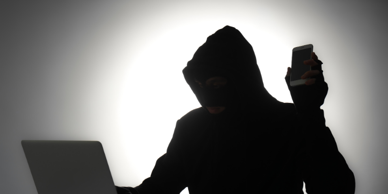 Silhouette of a male fraudster with a laptop and mobile phone on gray background