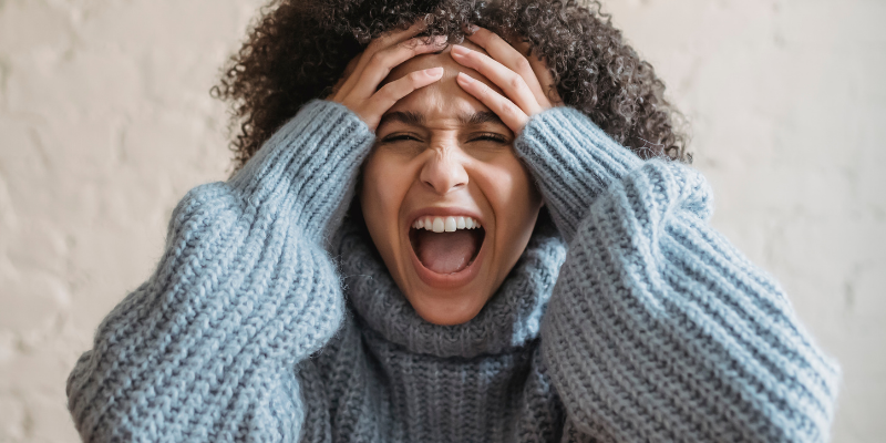 Upset woman in a cozy sweater screaming in a room with neutral background