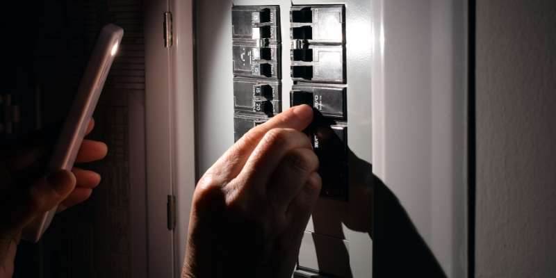 Person using a cell phone flashlight while switching on electrical breakers during a power outage