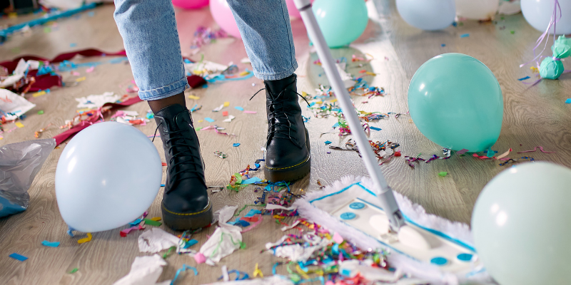 Woman with push broom cleaning up confetti and balloons from the floor after a party