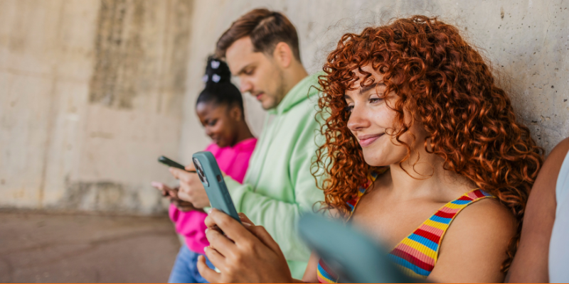 Young diverse people standing against a concrete wall engrossed in their mobile phones