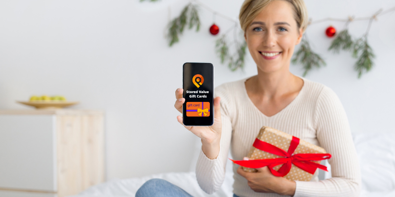 Woman holding a small, wrapped gift and holding up a mobile phone with a minimalist holiday background
